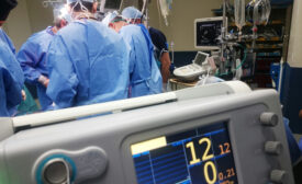 Medical Device Reliability - a cropped image of the vital monitor in the surgery room, medical staff in the background.