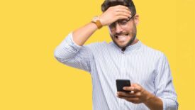 Young man texting using smartphone over isolated background stressed with hand on head.