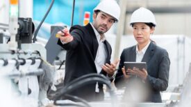 Senior official woman and male architectural engineer talking, wearing suits and safety hats.