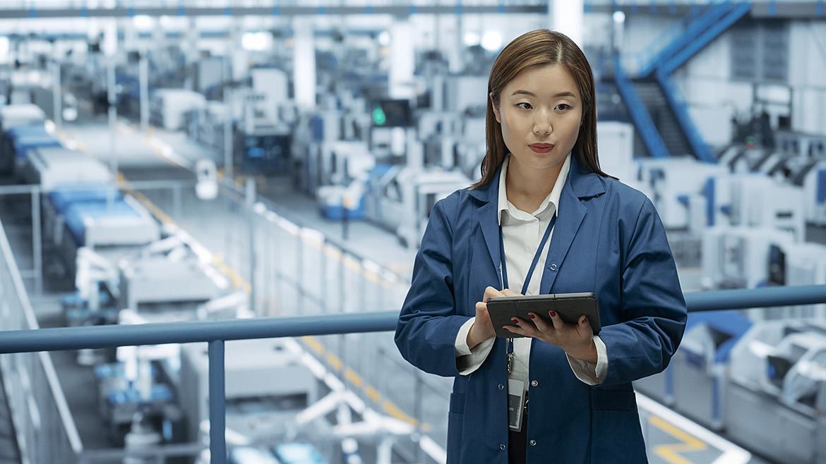 Engineer Monitoring and Analyzing Conditions at a Modern Electronics Factory with Automated Robot Hands Working with the Help of Artificial Intelligence Software.