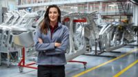 Portrait of female engineer, with crossed arms, standing against car chassis.