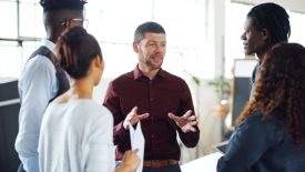 A man talking to a group of young people in a room.