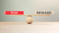 Wooden Seesaw Scale and Risk and Reward Written Wooden Blocks Sitting on Wood Surface in Front of Defocused Background