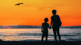 Mother Holding son standing beach in sunrise