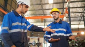 Angry engineer boss scolding young engineers for their mistake standing in the CNC manufacturing factory. Negative boss yelling employee during work. Man standing and feeling bad. Industrial concept.