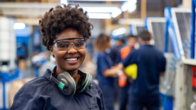 Female employee working at a solar panel factory wearing protective workwear and looking at the camera smiling.