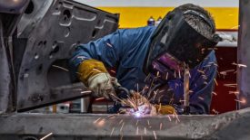 Man is welding vintage Porsche car frame with sparks flying.