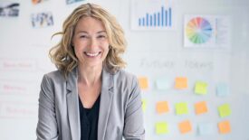 Smiling businesswoman standing in front of a whiteboard with charts and sticky notes.