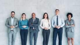 Group of business persons standing against a wall.