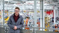 Male engineer leaning on railing in car plant.