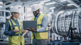 Two Professional Heavy Industry Engineers Wearing Safety Uniform and Hard Hats Working on Laptop Computer.