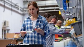 Woman in a line with other workers, checking and testing industrial equipment cables in a large electronics wire and cable manufacturing plant.