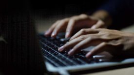 Close up of a man's hands on keyboard of lap top in the dark room.