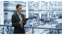 Female engineer monitoring and analyzing conditions at a modern tech electronics factory using a tablet. 