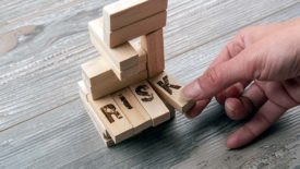 Hand taking the "K" block from wooden blocks tower. The "K" is part of four long blocks that say "RISK".