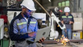 Mechanical engineer holding a laptop, doing maintenance work, while standing over the robotic welding machine.