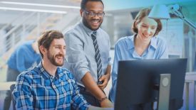 Three office workers, smiling and looking at a computer.