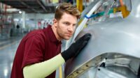 Engineer touching a car part during inspection in a car factory.