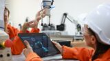 Female maintenance engineer working with a digital tablet and robotic arm in lab.