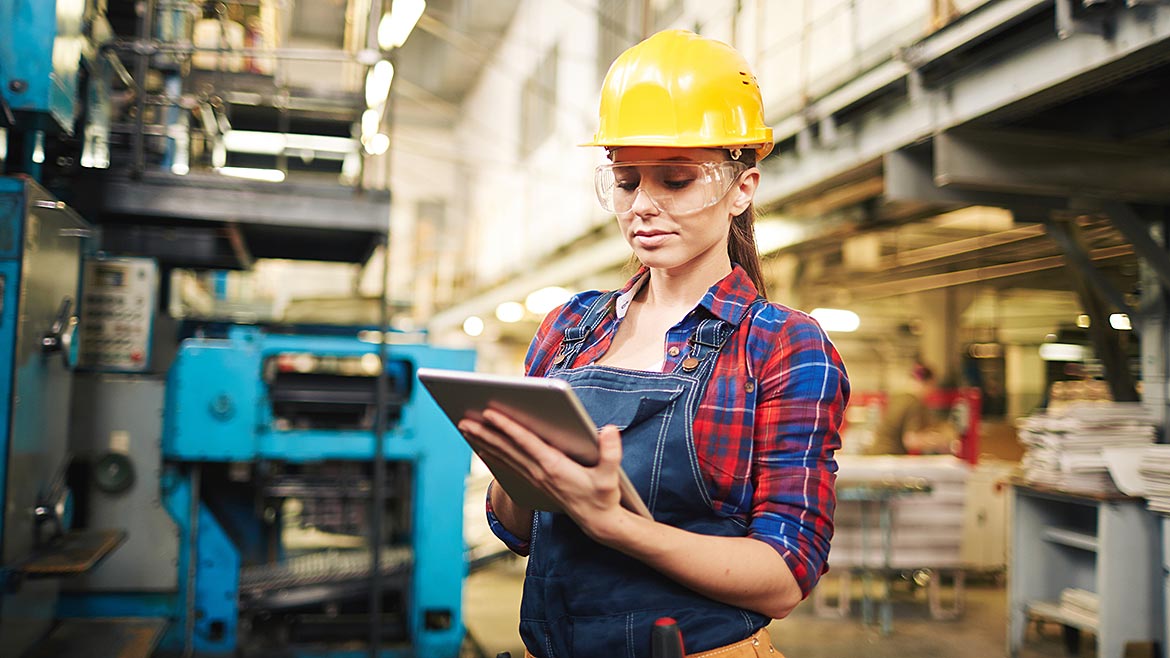 Female worker in safety gear and using a tablet in a plant.