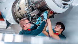 Two young male aircraft maintenance mechanics checking and inspecting an airplane jet engine in the hangar before the flight.