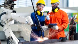 Male and female technicians using a tablet and watching a robot arm system welding.